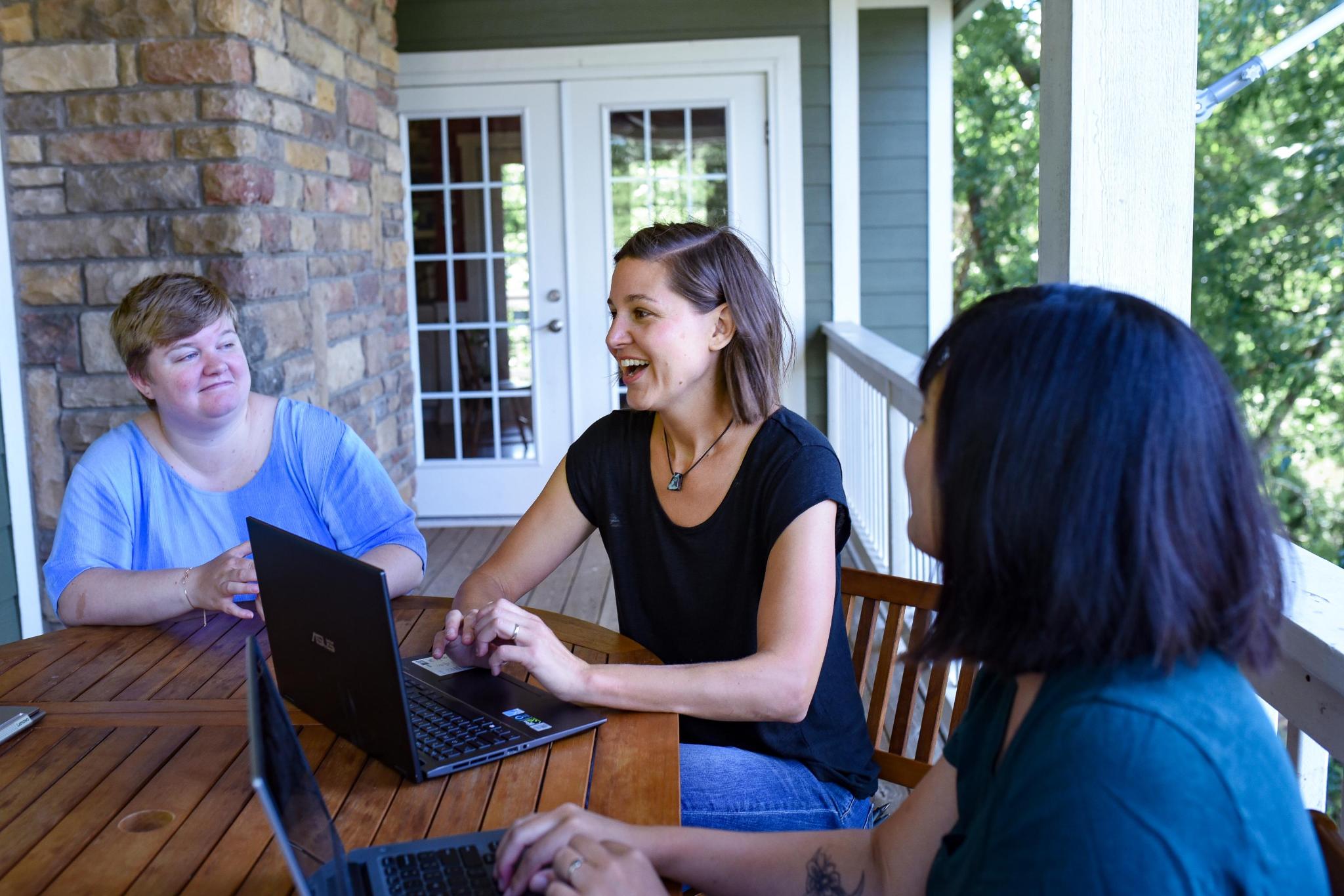 Three adults having a conversation around a table outdoors