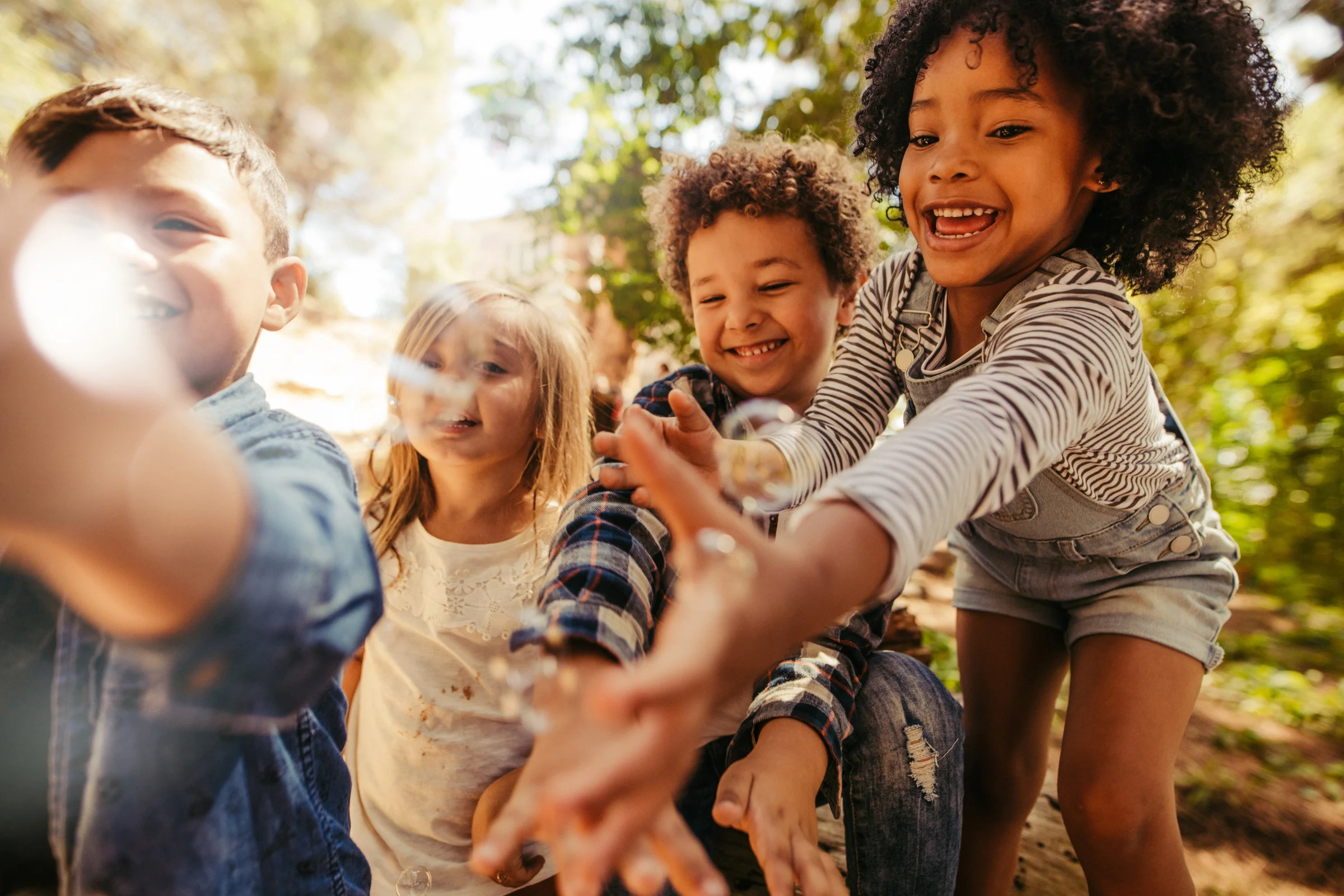 A group of 4 young children reaching their hands out to catch bubbles